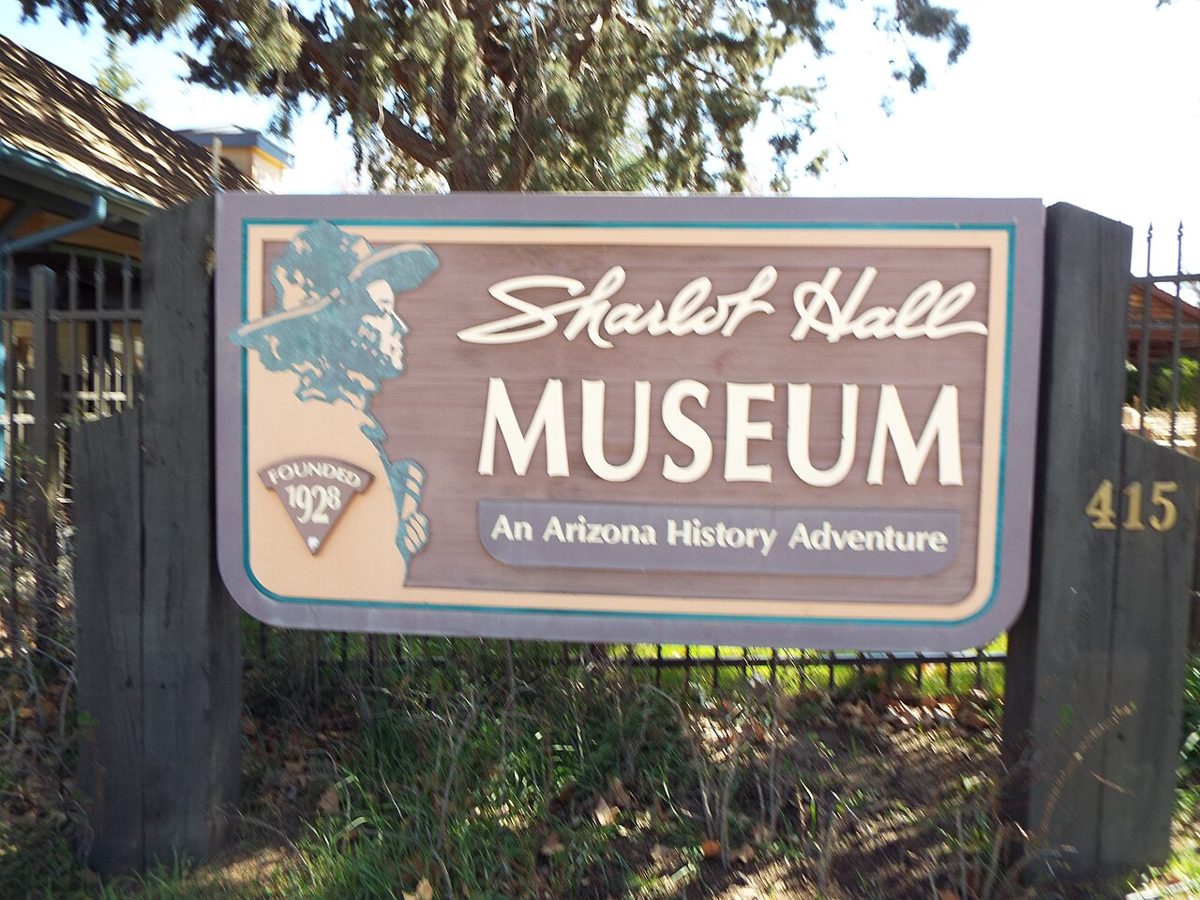 Carved wooden entrance sign reading 'Sharlot Hall Museum — An Arizona History Adventure', with a profile of a woman in a hat, 'Founded 1928', and the street number 415, in front of an iron fence.